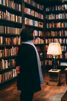 A woman in a library surrounded by bookshelves and a warm lamp light.