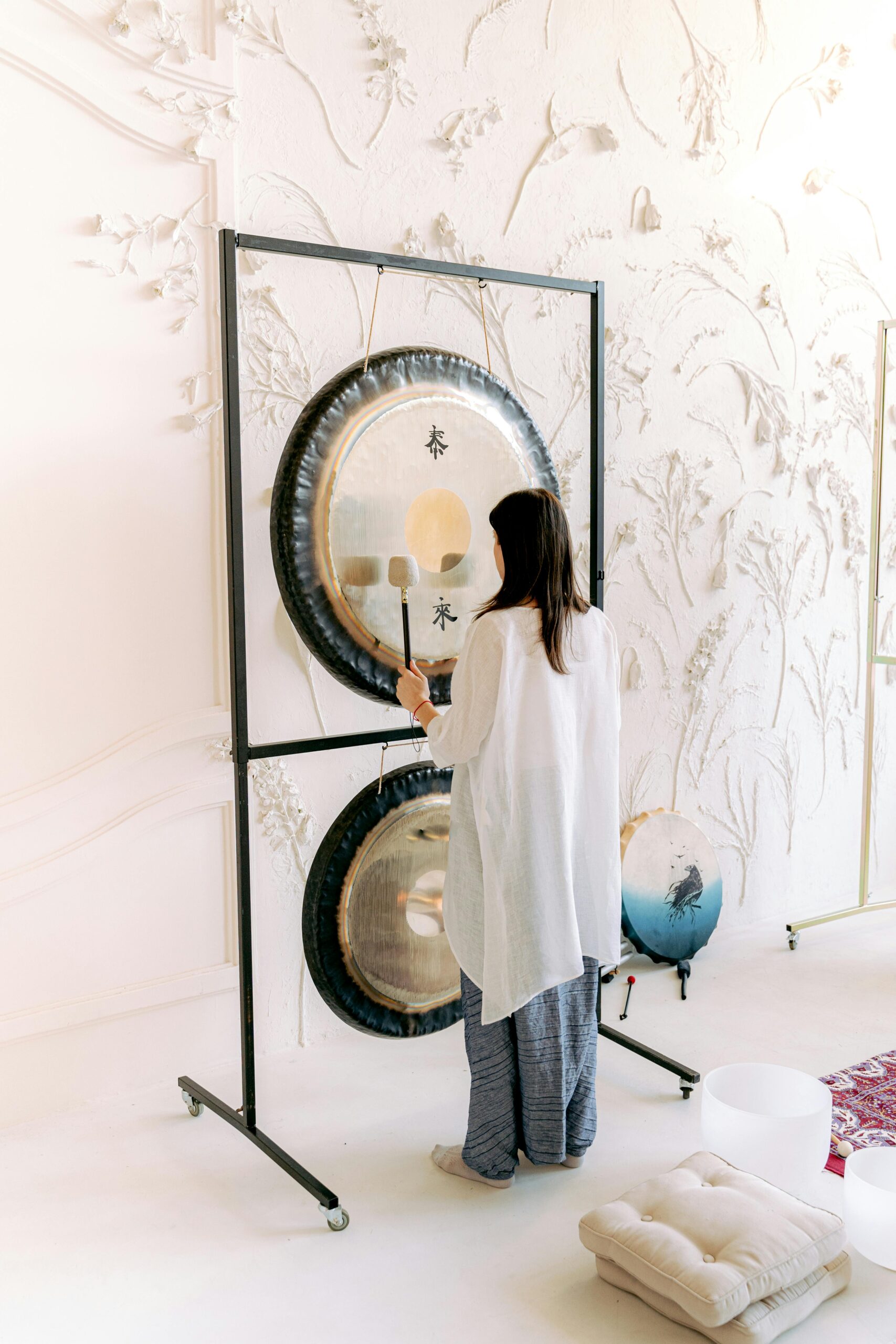 A woman engaged in sound healing therapy using a gong in a serene indoor setting.