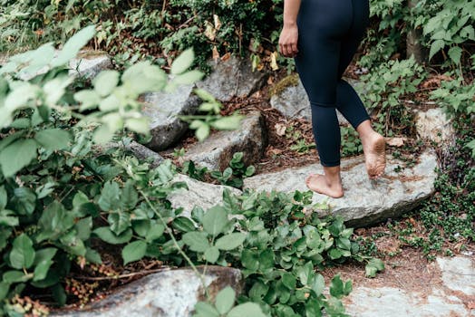 Adult walking barefoot on a rocky path surrounded by greenery, embracing nature's connection.